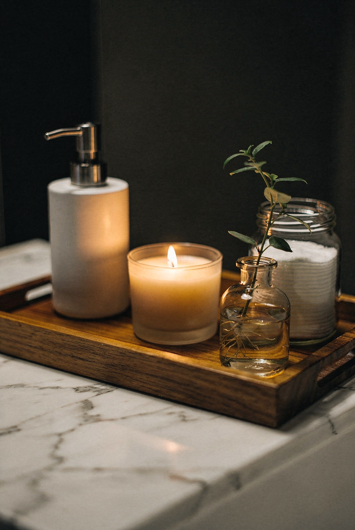 Wooden vanity tray with soap dispenser candle and jar, bathroom counter styling, warm moody lighting, cinematic interior