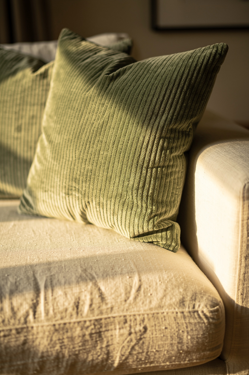 Sage green corduroy and cream linen throw pillows layered on a sunlit sofa corner with dried pampas grass arrangement on the side table